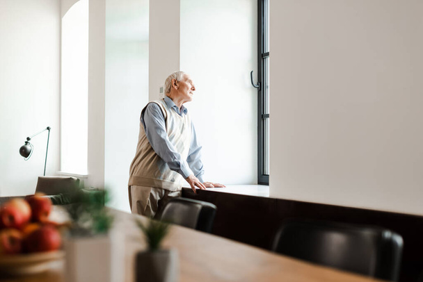 upset elderly man standing near window during quarantine, selective focus - Zdjęcie, obraz