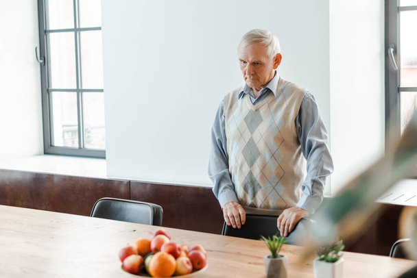 одинокий пожилой человек, стоящий за столом с фруктами во время карантина
  - Фото, изображение