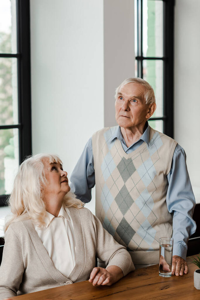 upset elderly couple with glass of water at home on self isolation - Φωτογραφία, εικόνα