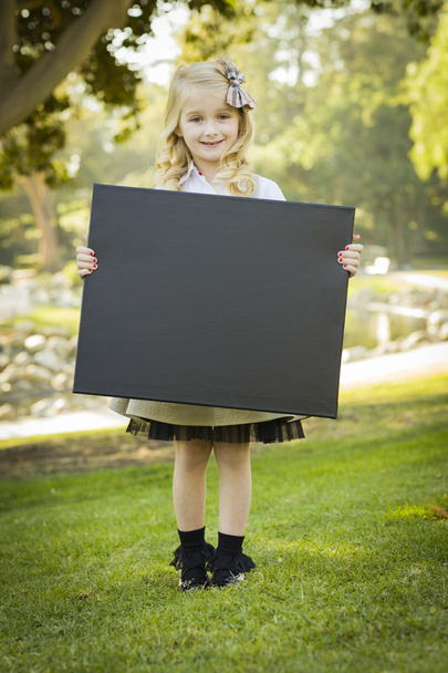 χαριτωμένο ξανθό κοριτσάκι που κρατάει ένα μαύρο πίνακα κιμωλίας σε εξωτερικούς χώρους - Φωτογραφία, εικόνα