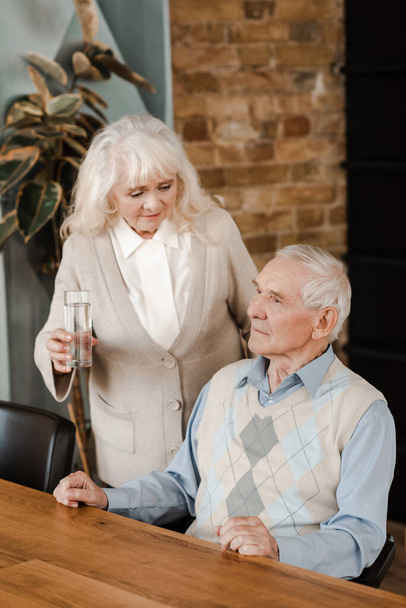 старша дружина і хворий чоловік зі склянкою води вдома під час карантину
 - Фото, зображення
