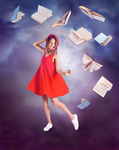Piękna młoda kobieta w czerwonej sukience taniec i latające książki na tle koloru  - Zdjęcie, obraz