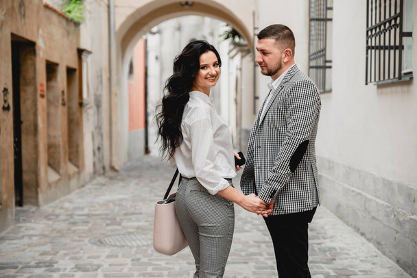 Charming girl with long brown hair and a man with a beard kissing on the background of the morning city. Newlyweds on their wedding day - Foto, imagen