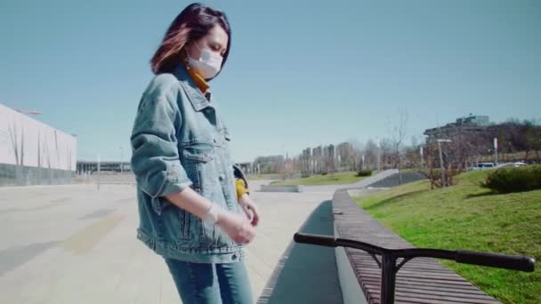 Junge Asiatin in medizinischer Maske mit Tretroller benutzt Smartphone im Sommerpark - Filmmaterial, Video