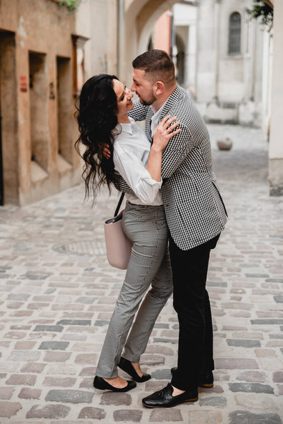 Charming girl with long brown hair and a man with a beard kissing on the background of the morning city. Newlyweds on their wedding day - Foto, Bild