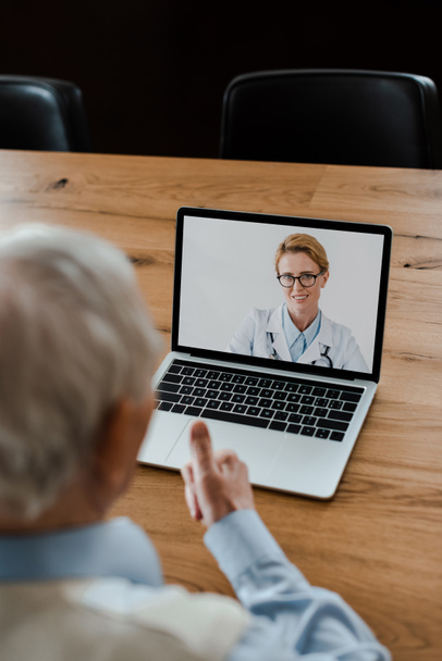 visão cortada de homem idoso mostrando polegar para cima e ter um bate-papo de vídeo com médico sorridente feminino durante o auto-isolamento
 - Foto, Imagem