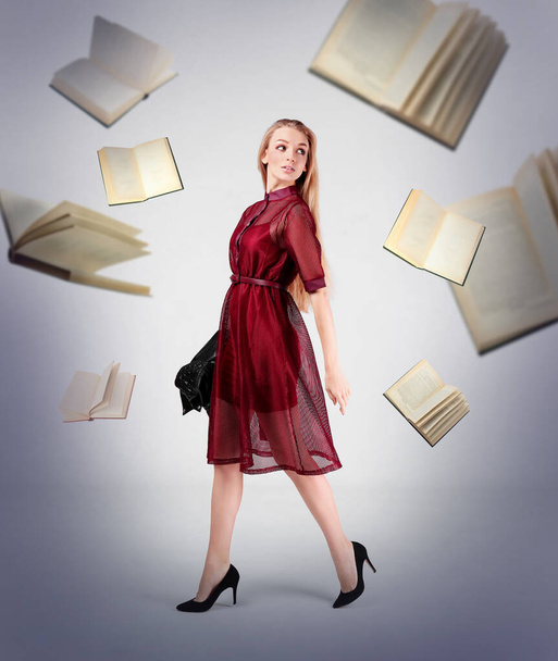 Young stylish woman in dress and flying books on light background - Foto, afbeelding