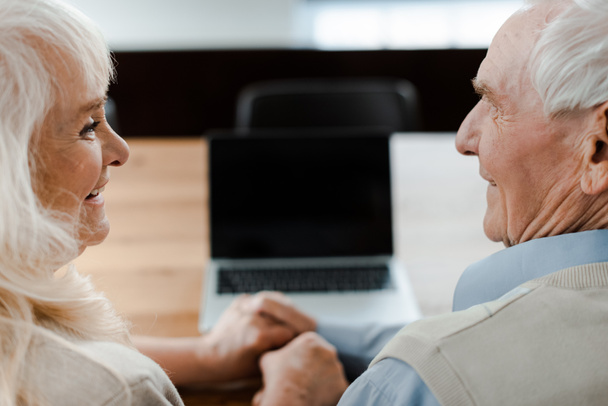 heureux couple âgé tenant la main tout en ayant appel vidéo sur ordinateur portable avec écran blanc à la maison pendant l'isolement personnel
 - Photo, image