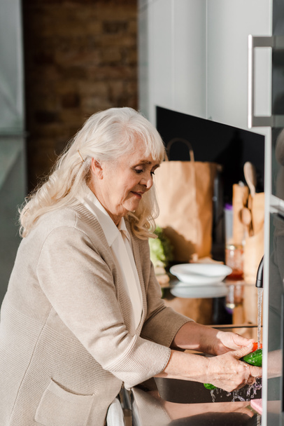 усміхнена літня жінка миє овочі на кухні
  - Фото, зображення