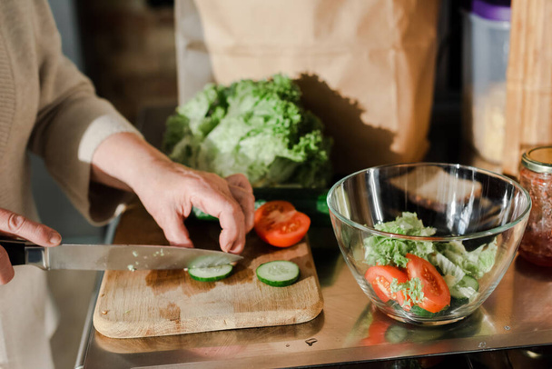 rajattu näkymä vanhempi nainen leikkaamalla vihanneksia aluksella salaattia keittiössä  - Valokuva, kuva