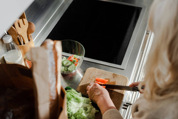 cropped view of elderly woman cutting vegetables on board for salad on kitchen  - Photo, image