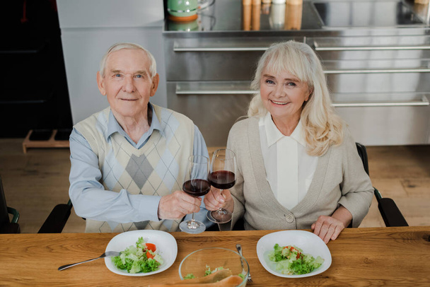 happy senior couple having dinner with wine and salad at home on self isolation - Foto, Bild