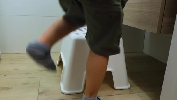 Το αγόρι μπαίνει στο μπάνιο στο σπίτι, σηκώνεται σε μια καρέκλα. Στάση από παιδικά πόδια που υψώνονται στα δάχτυλα των ποδιών σε μια καρέκλα στο νεροχύτη. Έννοια υγιεινής - Πλάνα, βίντεο