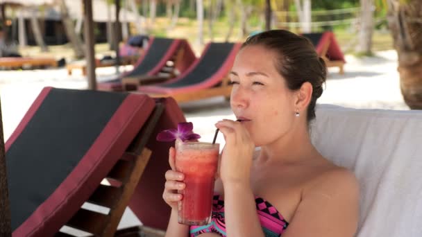 dame ligt op zonnebank en drinkt heerlijke cocktail onder schuur - Video