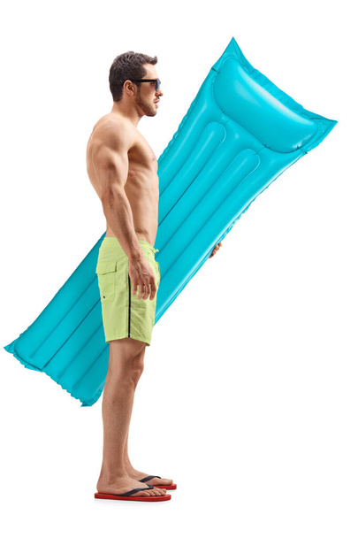 Full length profile shot of a young man in swimming shorts with an water air mattress isolated on white background - Foto, immagini