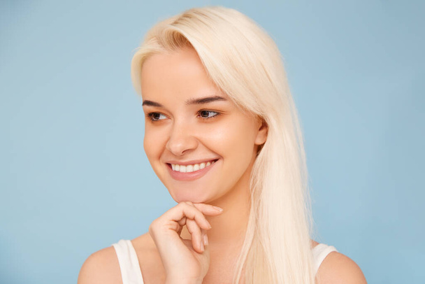 Beautiful young girl smiling closeup against blue background, white teeth, clean skin. - Fotografie, Obrázek