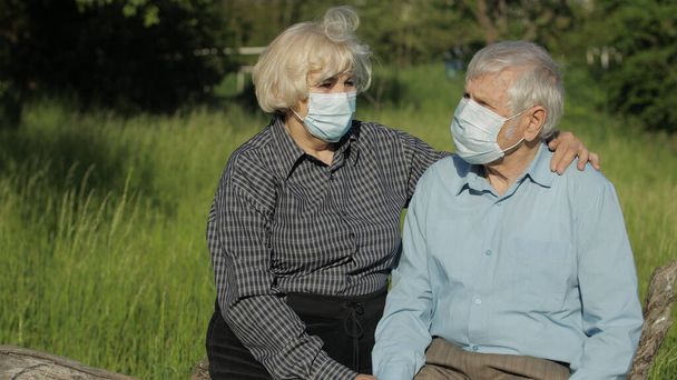 Casal sênior em máscaras médicas durante a quarentena do coronavírus COVID-19 no parque
 - Foto, Imagem