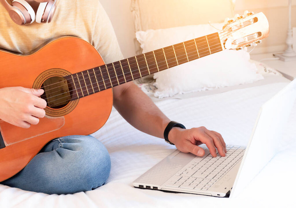 Kavkazský muž kontroluje svůj notebook, zatímco se učí hrát na kytaru on-line - Fotografie, Obrázek