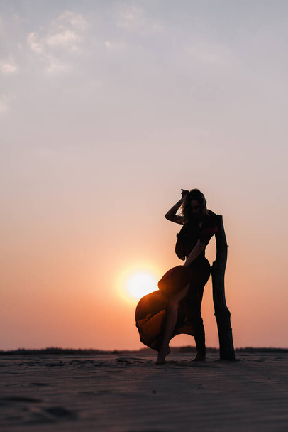 Silhouette of a girl in a red dress at sunset in the desert  - Foto, afbeelding