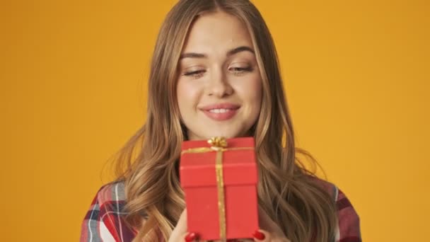 Young happy positive girl isolated over yellow wall background holding present box - Filmagem, Vídeo