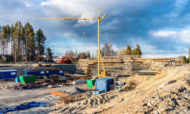 Foto der neuen Brückenbaustelle mit Holzkonstruktion zur weiteren Betonierung. Gelber Kranturm, blaue Wolken, tiefer Graben. Viele Baumaterialien - Stahl- und Holzteile - Foto, Bild