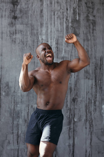 black man boxer rejoices victory after the fight. Happy athlete raises his hands up - 写真・画像