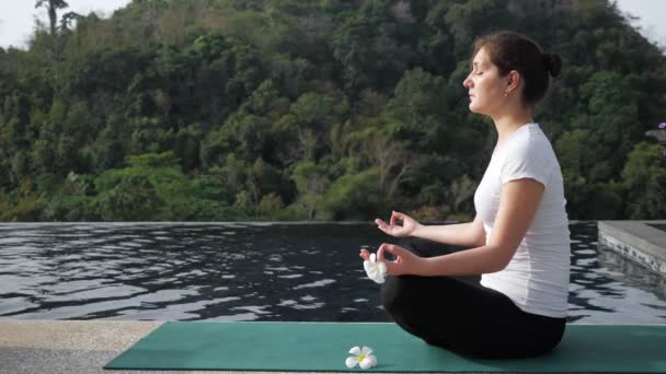 mujer joven se sienta en una posición de loto cerca de la piscina de la azotea
 - Metraje, vídeo