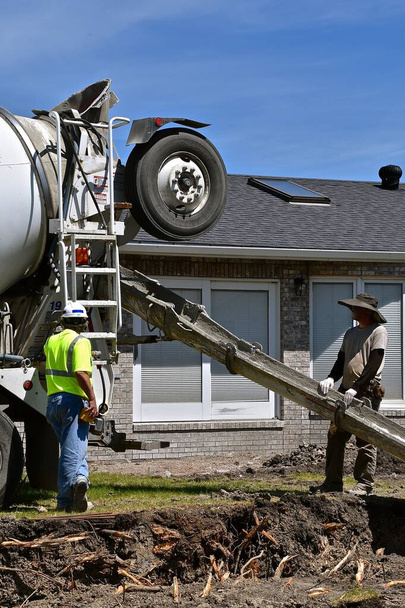 Azonosítatlan munkások ellenőrzik az ernyőt, ahol nedves beton hagyja el a kész keverék teherautó. - Fotó, kép