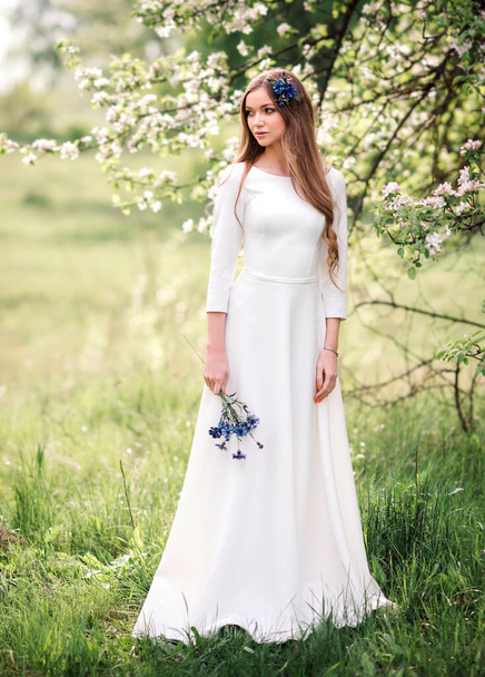 Beautiful young girl with long hair in a white dress in a summer blooming garden - Foto, Imagen