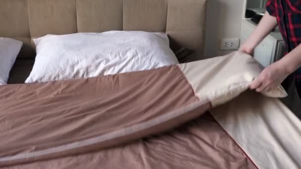 Gömlekli kadın otel odasında kahverengi battaniyeyle yatağı örtüyor. - Video, Çekim