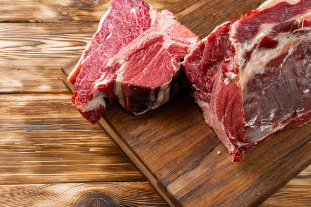 Raw T-bone steak with herbs on wooden board - Фото, изображение