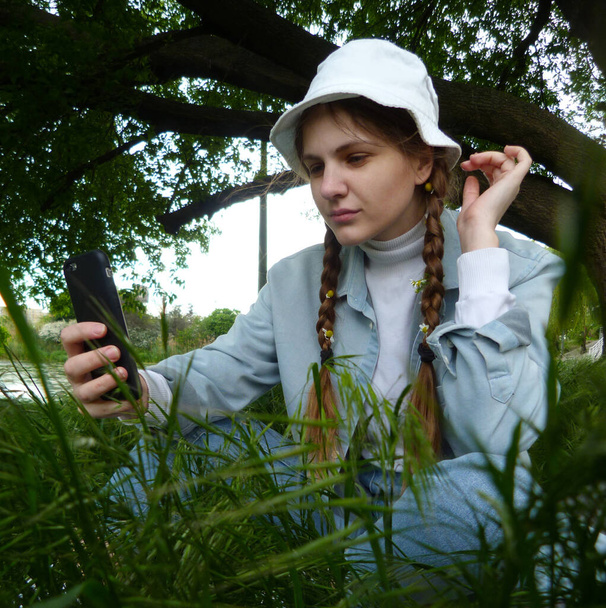 Krásná dívka fotografování sebe, sedí na zelené trávě, se stromem na pozadí - Fotografie, Obrázek