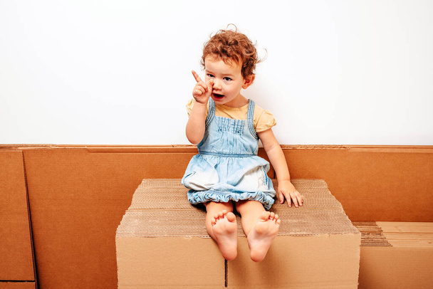 Girl plays alone on cardboard boxes with funny expressions. - Photo, Image