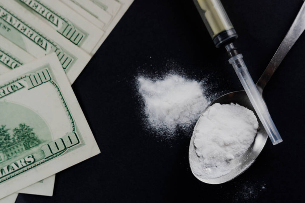 真っ黒な背景にスプーンやお金で粉末状の物質、シリンジ。薬物中毒やヘロインなどの薬物使用の概念 - 写真・画像