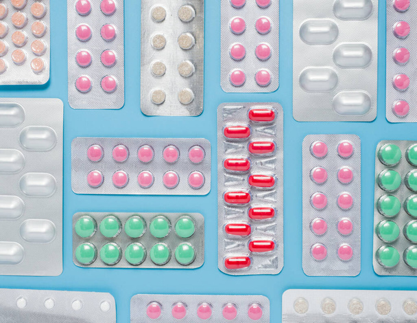 Different colorful pills tabtes iv blisters for treatment on blue background, flat lay. - Photo, image