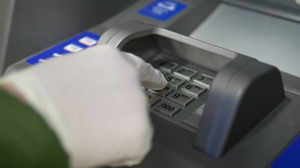 ręka w rękawiczce klika na guziki bankomatu, wchodzi hasło zbliżeniowe w banku, koronawirus w miejscu publicznym - Materiał filmowy, wideo
