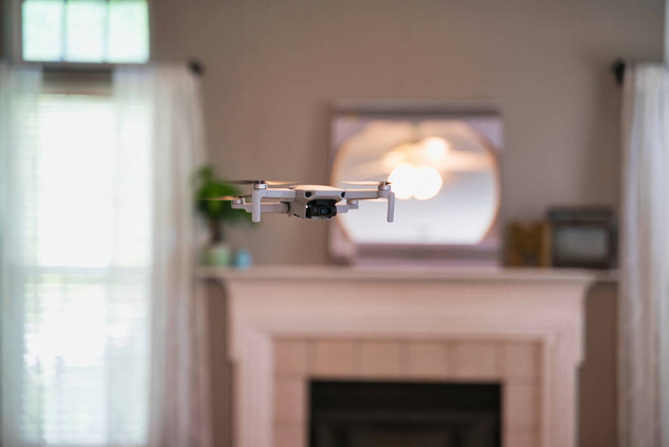 Drone volando en el interior con ventana visible en el fondo. Drone blanco flotando dentro de la casa
. - Foto, imagen