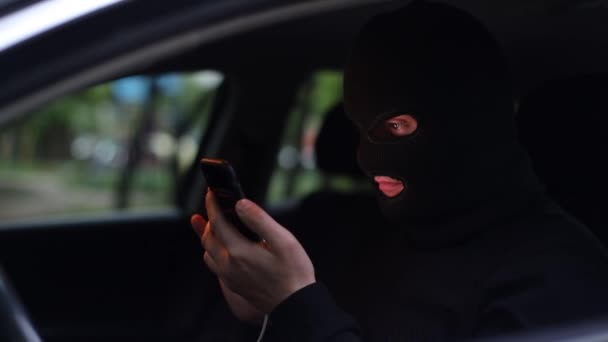 Egy férfi maszkban, egy fiatal bűnöző okostelefonnal a kezében. - Felvétel, videó