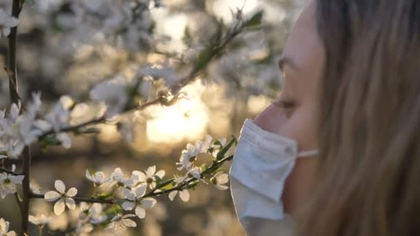 Mädchen entfernt medizinische Maske und erschnüffelt blühenden Apfel- oder Kirschbaum bei Sonnenuntergang aus nächster Nähe - Filmmaterial, Video