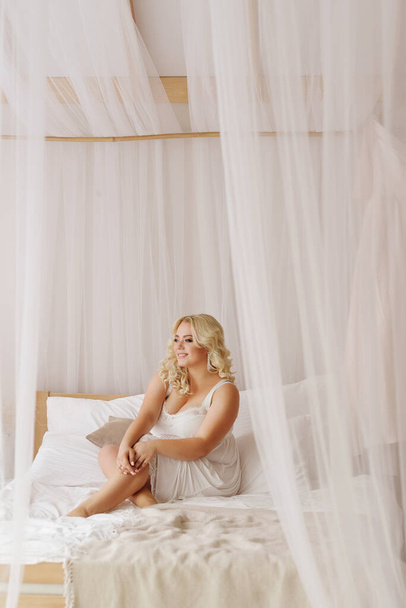 blonde fille plus taille modèle en blanc lingerie portrait Bali matin mariée couleur sourit coquettishly assis dans une lumière intérieure gros seins
 - Photo, image