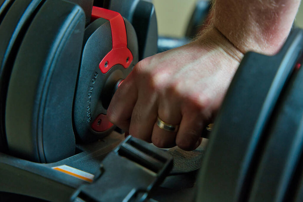 Mancuernas ajustables de agarre manual para hacer ejercicio en casa. mano masculina con anillo visible
. - Foto, Imagen