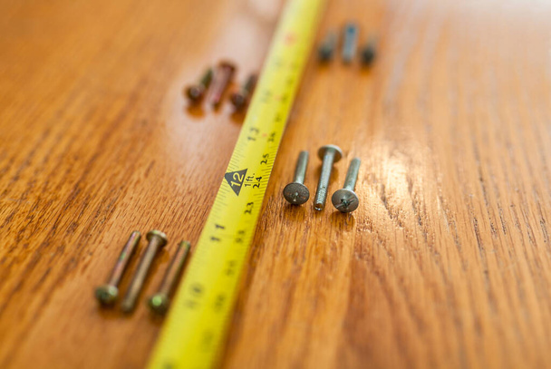 4 sets of 3 screws and a tape measure on wood - Fotó, kép