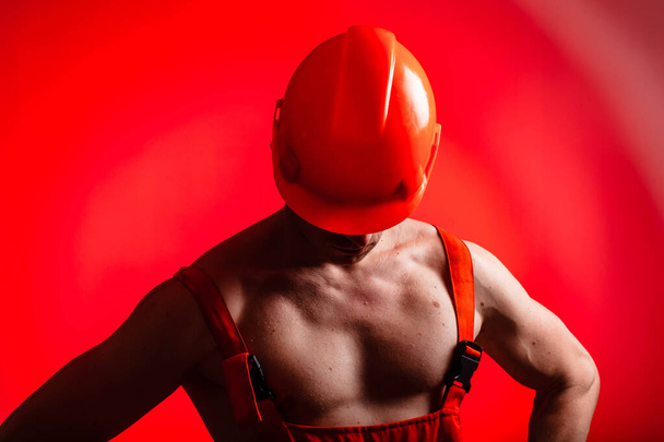 Sexy builder on a red background. Builder with a helmet on his head. Sexy builder. Pumped arms and back. - Fotoğraf, Görsel