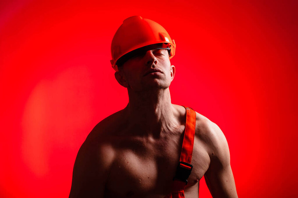 Constructor sexy sobre un fondo rojo. Constructor con un casco en la cabeza. Constructor sexy. Brazos bombeados y espalda
. - Foto, imagen