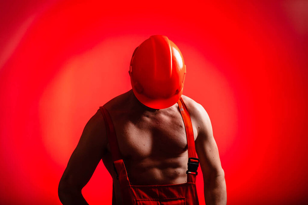 Sexy Bauarbeiter auf rotem Hintergrund. Bauarbeiter mit Helm auf dem Kopf. Sexy Bauunternehmerin. Arme und Rücken gepumpt. - Foto, Bild