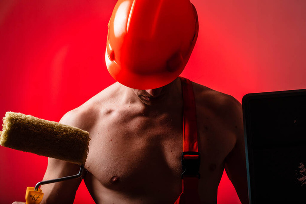 Sexy builder on a red background. Builder with a helmet on his head. Sexy builder. Pumped arms and back. - Fotó, kép