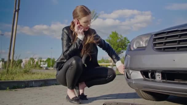 Trafik kazasından sonra genç ve tatlı bir kadın telefon görüşmesi yapıyor. Arızalı bir arabanın önünde duran ve tamirci ya da sigortacı çağıran genç bir kadın. Yol kenarı yardım kavramı. - Video, Çekim