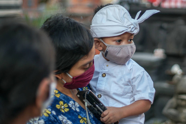 La mère et l'enfant balinais portent des vêtements traditionnels balinais pendant la pandémie de corona ou covid-19. Ils utilisent tous les deux des masques pour se protéger contre les attaques de virus. - Photo, image