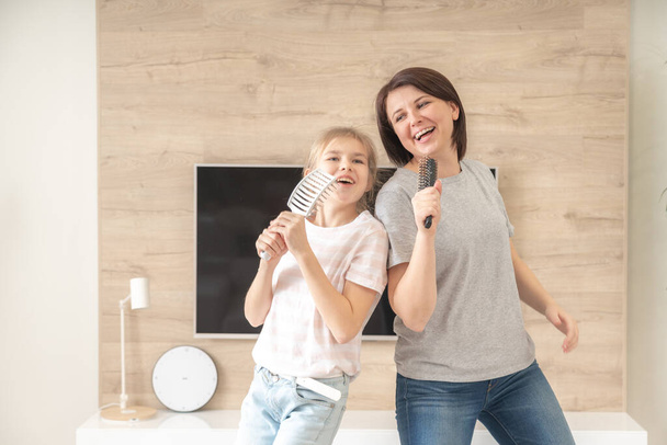 Happy family young adult mother and cute teen daughter having fun singing karaoke song in hairbrushes. mother laughing enjoying funny lifestyle activity with teenage girl at home together. - Φωτογραφία, εικόνα