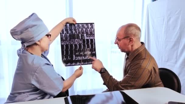 Eine Ärztin stellt bei einem Mann nach den Ergebnissen der Magnetresonanztomographie der Wirbelsäule eine Diagnose. Gesamtplan - Filmmaterial, Video